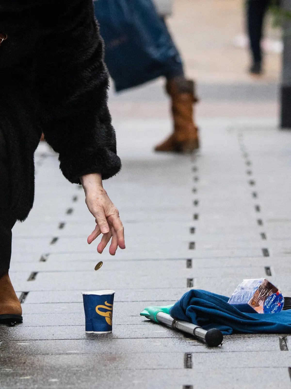 ARCHIV - 27.12.2017, Hessen, Wiesbaden: Eine Frau wirft einem Bettler ein Geldstück in einen Becher. Menschen ohne festen Wohnsitz sind nicht unbedingt die Wunschkunden vieler Banken. Mittlerweile haben sie aber das Recht auf ein Konto. (Zu dpa «Studie: Konten für Wohnungslose und Geflüchtete oft besonders teuer») Foto: Andreas Arnold/dpa +++ dpa-Bildfunk +++