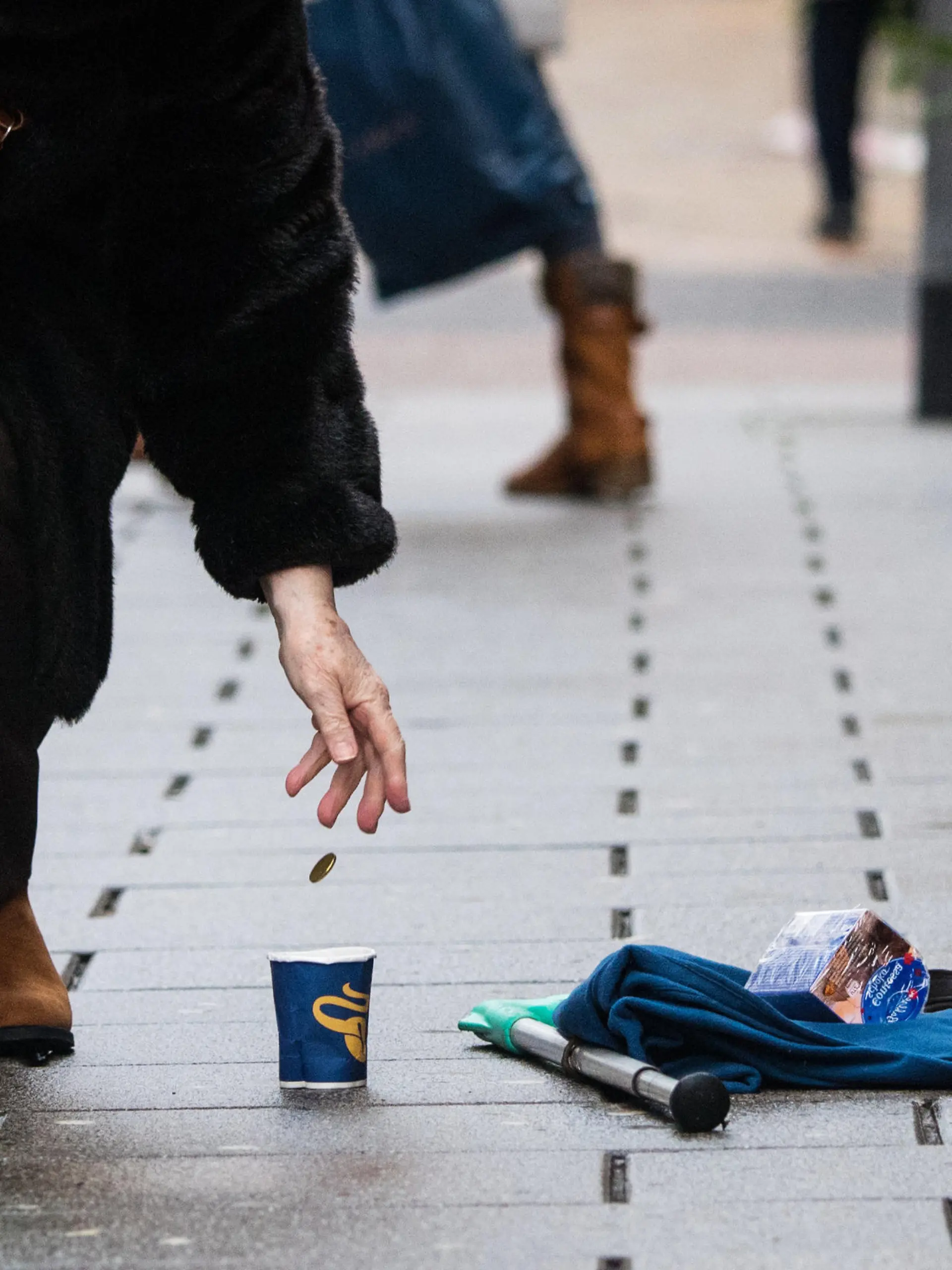 ARCHIV - 27.12.2017, Hessen, Wiesbaden: Eine Frau wirft einem Bettler ein Geldstück in einen Becher. Menschen ohne festen Wohnsitz sind nicht unbedingt die Wunschkunden vieler Banken. Mittlerweile haben sie aber das Recht auf ein Konto. (Zu dpa «Studie: Konten für Wohnungslose und Geflüchtete oft besonders teuer») Foto: Andreas Arnold/dpa +++ dpa-Bildfunk +++