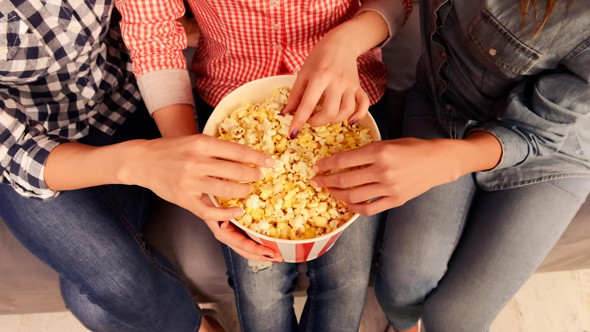 Close up photo of three women sitting on couch and eating popcorn