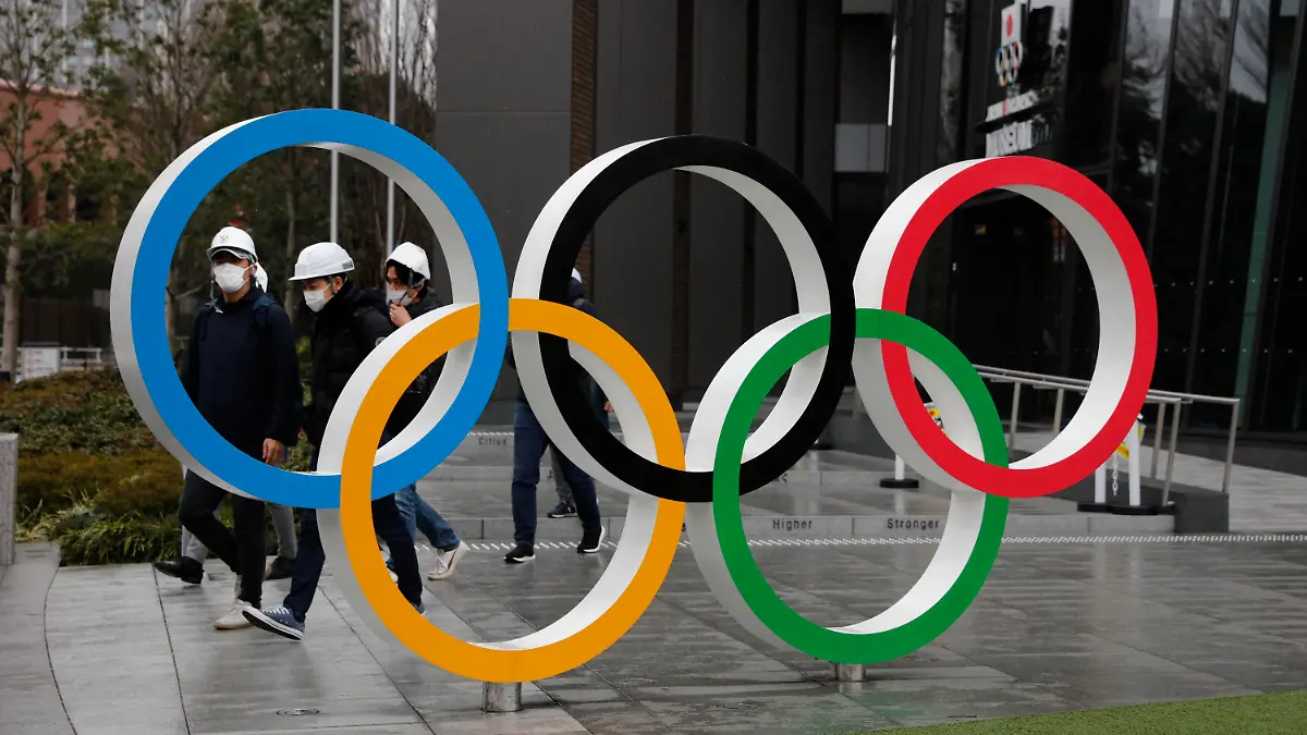 04.03.2020, Japan, Tokio: Menschen tragen einen Mundschutz, während sie an den Olympischen Ringen in der Nähe des neuen Nationalstadions vorbei. Organisierte Reisen zu den Olympischen Spielen in Tokio sind aus Angst vor dem Coronavirus derzeit noch nicht sehr gefragt. Foto: Jae C. Hong/AP/dpa +++ dpa-Bildfunk +++