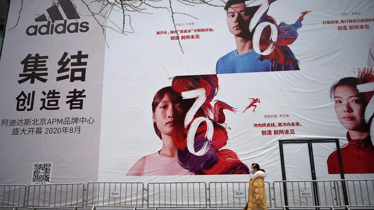 FILE PHOTO: A woman wearing a face mask walks past a banner advertising new Adidas store, as the country is hit by an outbreak of the novel coronavirus, in Beijing, China February 20, 2020. REUTERS/Tingshu Wang/File Photo