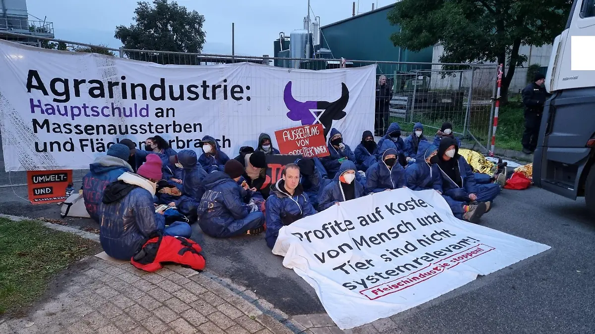 26.09.2022, Niedersachsen, Badbergen: Demonstranten sitzen bei einer unangemeldeten Protestaktion vor einem Betrieb des Schlachtkonzerns Tönnies. Für die Demonstration verantwortlich ist nach Angaben der Polizei «Gemeinsam gegen die Tierindustrie», eine Gruppe von Tierrechtsaktivisten. Die Aktivisten beschuldigten den Konzern in einer Mitteilung der Ausbeutung von Mensch und Tier sowie der Zerstörung von Klima und Natur. Foto: Ulf Zurlutter/Nord-West-Media TV /dpa +++ dpa-Bildfunk +++