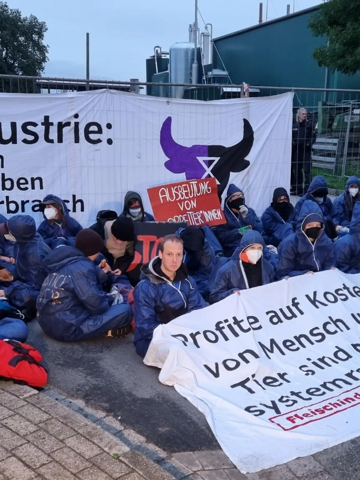 26.09.2022, Niedersachsen, Badbergen: Demonstranten sitzen bei einer unangemeldeten Protestaktion vor einem Betrieb des Schlachtkonzerns Tönnies. Für die Demonstration verantwortlich ist nach Angaben der Polizei «Gemeinsam gegen die Tierindustrie», eine Gruppe von Tierrechtsaktivisten. Die Aktivisten beschuldigten den Konzern in einer Mitteilung der Ausbeutung von Mensch und Tier sowie der Zerstörung von Klima und Natur. Foto: Ulf Zurlutter/Nord-West-Media TV /dpa +++ dpa-Bildfunk +++