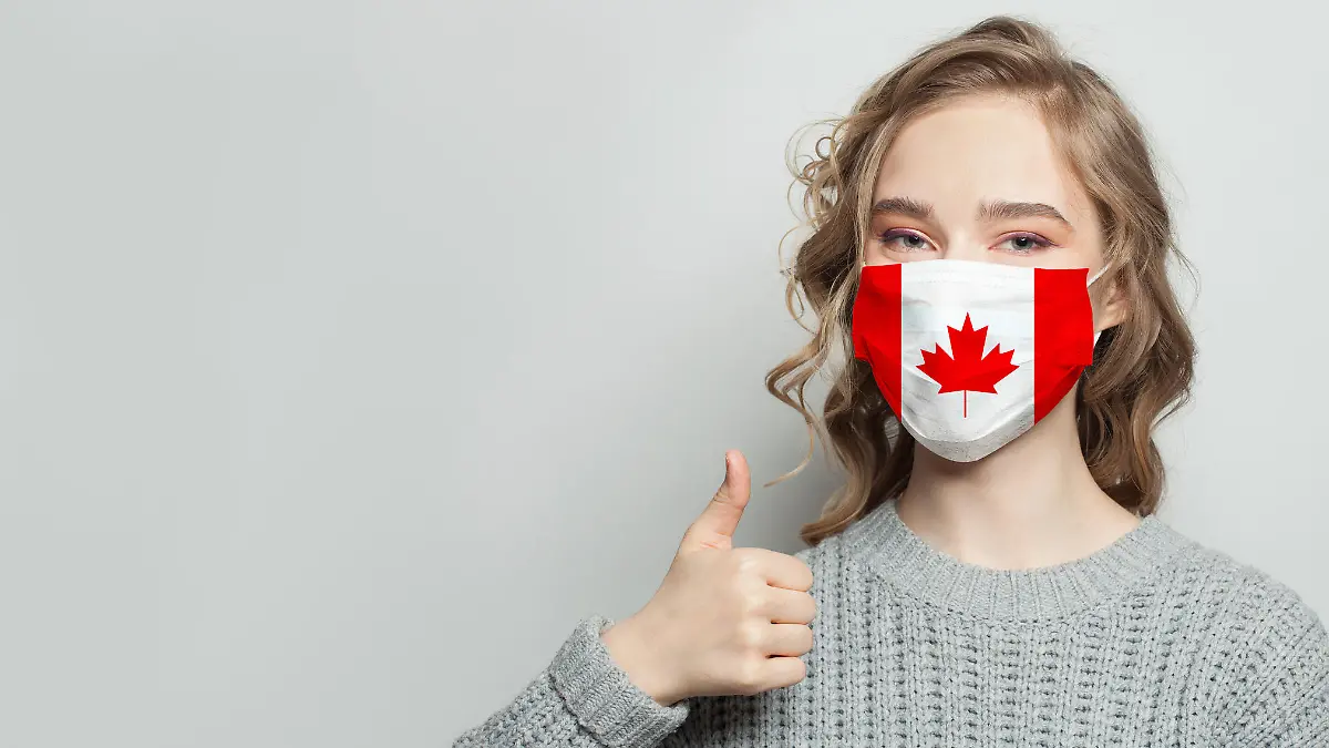 Frau mit Kanada-Flagge auf ihrer Maske hält Daumen hoch.