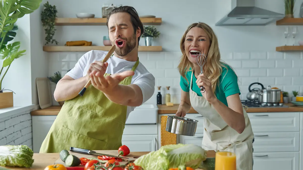 Playful couple having fun and singing while cooking together at the kitchen