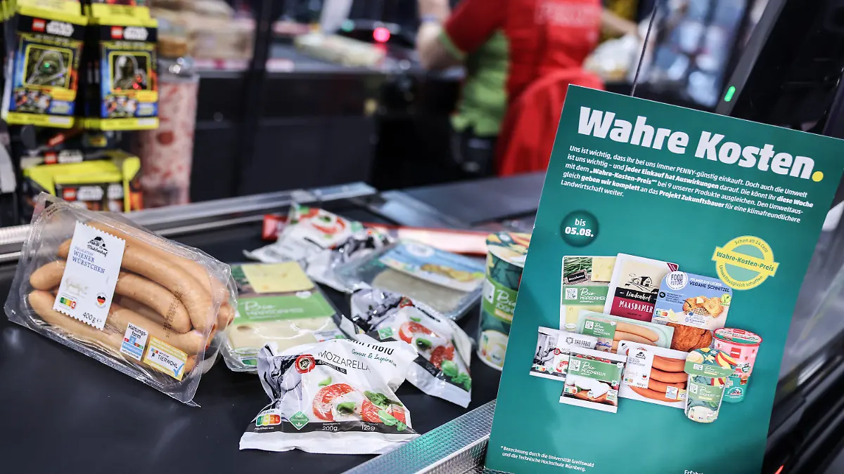PRODUKTION - 26.07.2023, Nordrhein-Westfalen, Köln: Produkte deren Preis mit den verdeckte Kosten angepasst wurden, liegen an der Kasse. Penny sorgt ab Montag (31.0.07.2023) für einen Preisschock der eigenen Art. Für neun Produkte kassiert das Unternehmen die «wahren Preise». Dabei werden auch verdeckte Kosten etwa für Umweltverschmutzung bei der Produktion berücksichtigt. (Zu dpa: «Discounter-Experiment: Wie teuer Lebensmittel eigentlich sei müssten») Foto: Oliver Berg/dpa +++ dpa-Bildfunk +++