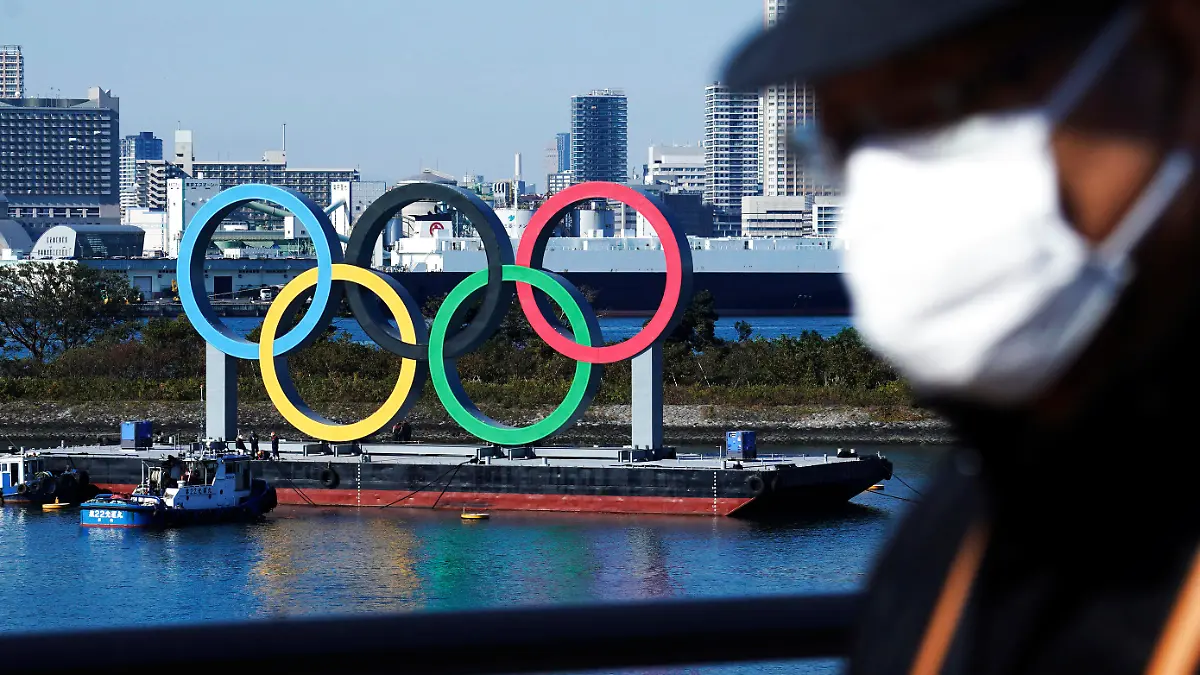 ARCHIV - 01.12.2020, Japan, Tokio: Ein Mann, der eine schützende Gesichtsmaske trägt, um die Ausbreitung des Coronavirus einzudämmen, geht nahe der Olympischen Ringe in der Bucht von Tokio, nachdem diese vor vier Monaten zur Wartung entfernt wurden, kurz nachdem die Olympischen Spiele in Tokio wegen der Corona-Pandemie auf nächstes Jahr verschoben worden waren. Die Olympischen Spiele sollen vom 23. Juli bis zum 8. August 2021 in Tokio stattfinden. (zu dpa: Zu 100 Tage vor Olympia am 14. April) Foto: Eugene Hoshiko/AP/dpa +++ dpa-Bildfunk +++