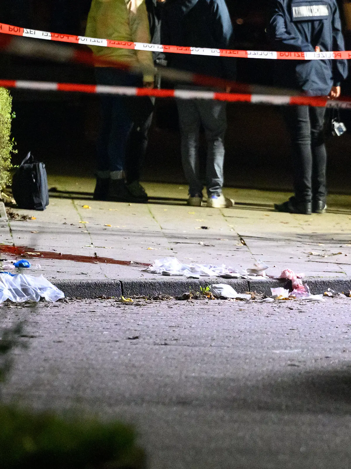 21.09.2022, Hamburg: Polizisten und Ermittler stehen am abgesperrten und ausgeleuchteten Tatort mit Blutspuren und Verbandsmaterial. Passanten haben in Hamburg-Veddel am Mittwochabend einen Mann mit Schussverletzungen am Kopf aufgefunden. Der Mann sei mit lebensgefährlichen Verletzungen in ein Krankenhaus gekommen, sagte ein Sprecher der Polizei Hamburg am frühen Donnerstagmorgen. Foto: Jonas Walzberg/dpa +++ dpa-Bildfunk +++
