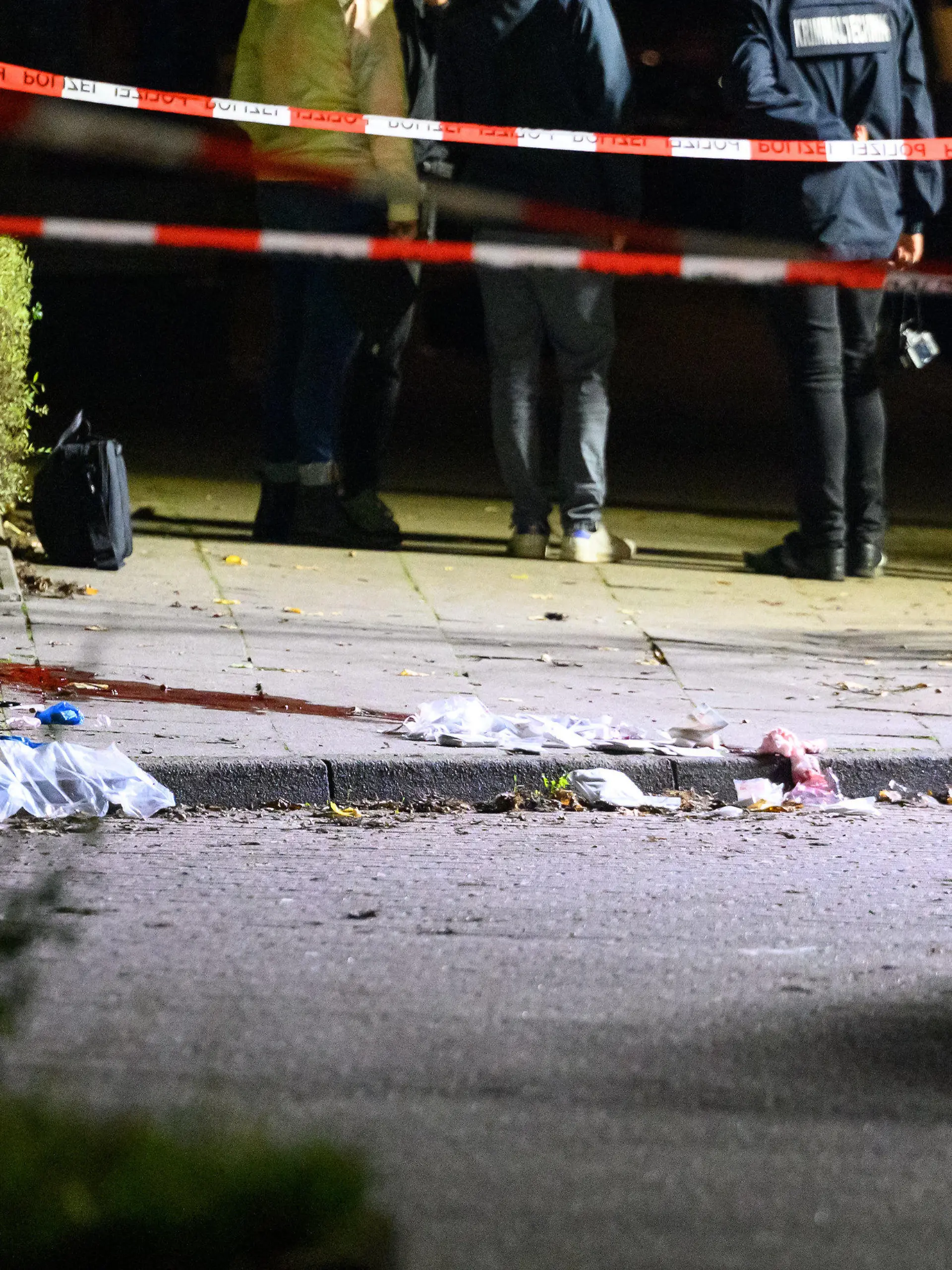 21.09.2022, Hamburg: Polizisten und Ermittler stehen am abgesperrten und ausgeleuchteten Tatort mit Blutspuren und Verbandsmaterial. Passanten haben in Hamburg-Veddel am Mittwochabend einen Mann mit Schussverletzungen am Kopf aufgefunden. Der Mann sei mit lebensgefährlichen Verletzungen in ein Krankenhaus gekommen, sagte ein Sprecher der Polizei Hamburg am frühen Donnerstagmorgen. Foto: Jonas Walzberg/dpa +++ dpa-Bildfunk +++