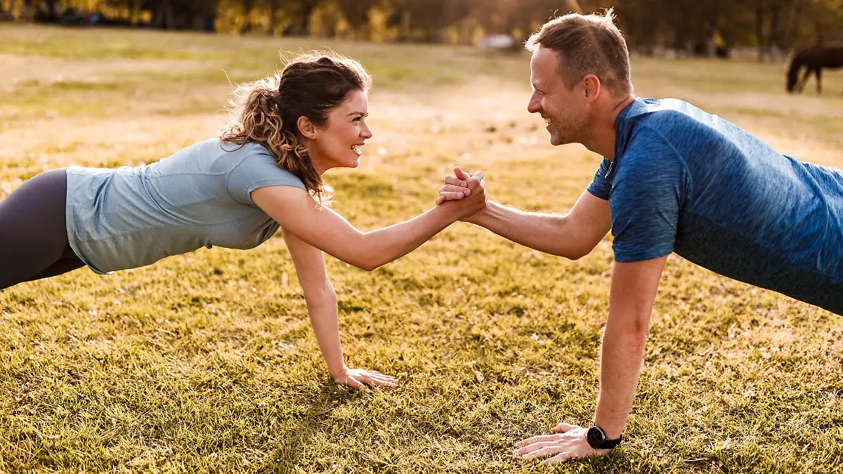 Happy couple of athletes holding hands while being in plank position in nature. Copy space.