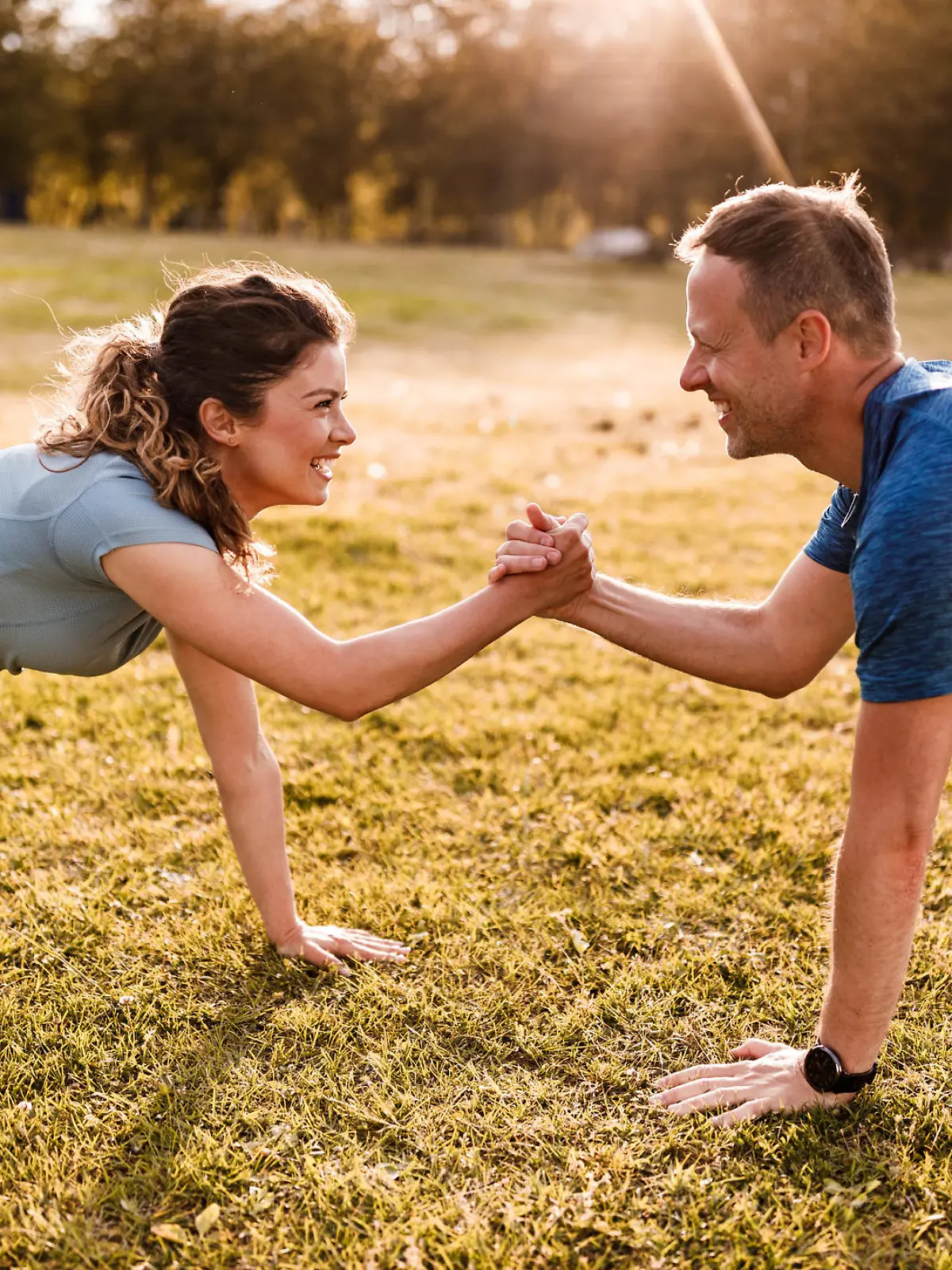 Happy couple of athletes holding hands while being in plank position in nature. Copy space.