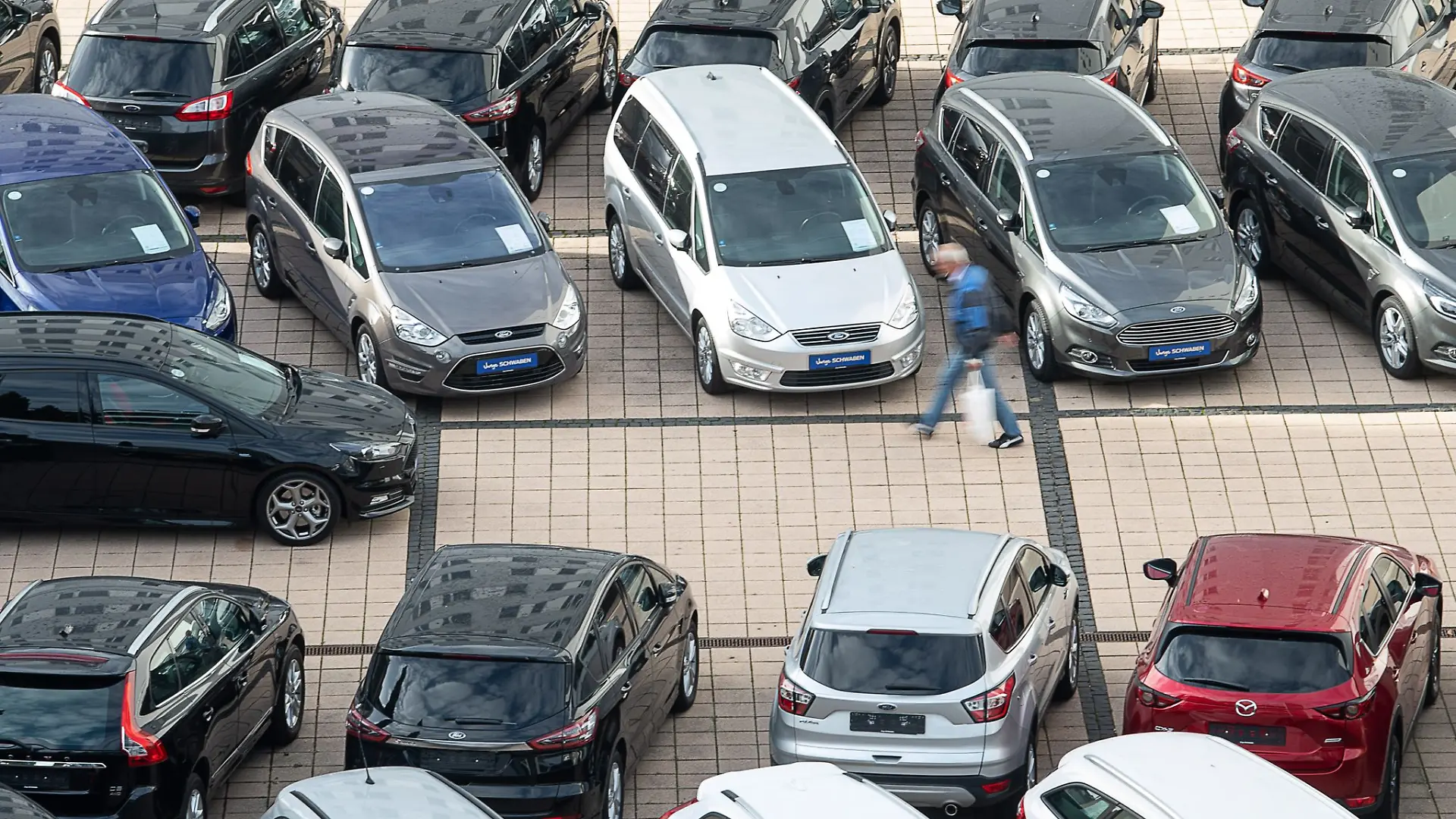 Ein Mann geht in einem Autohaus an Gebrauchtwagen vorbei.