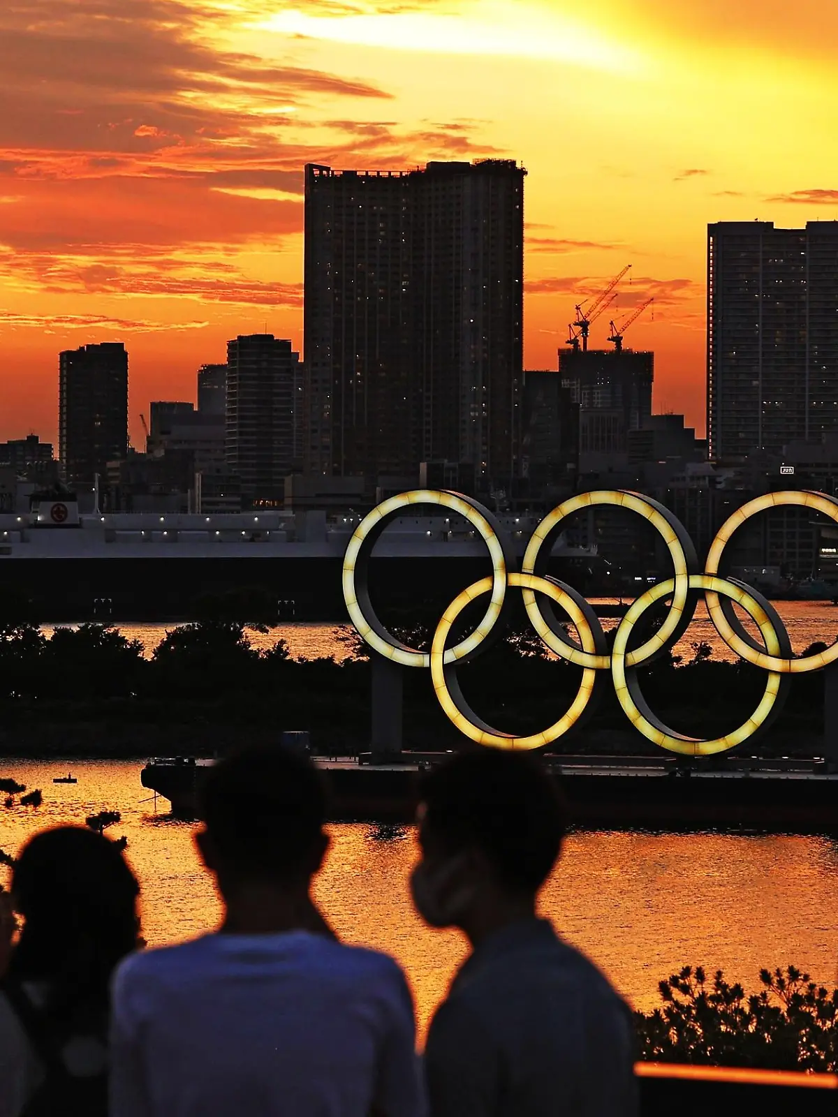 dpatopbilder - 21.07.2021, Japan, Tokio: Menschen schauen auf die bei Sonnenuntergang beleuchteten olympischen Ringe in der Bucht von Tokio. Foto: -/kyodo/dpa +++ dpa-Bildfunk +++