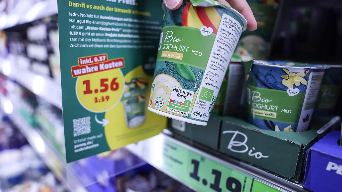 PRODUKTION - 26.07.2023, Nordrhein-Westfalen, Köln: Zwei Preisschilder hängen im Kühlregal vor einem Karton mit Bio Joghurt. Penny sorgt ab Montag (31.0.07.2023) für einen Preisschock der eigenen Art. Für neun Produkte kassiert das Unternehmen die «wahren Preise». Dabei werden auch verdeckte Kosten etwa für Umweltverschmutzung bei der Produktion berücksichtigt. (Zu dpa: «Discounter-Experiment: Wie teuer Lebensmittel eigentlich sei müssten») Foto: Oliver Berg/dpa +++ dpa-Bildfunk +++