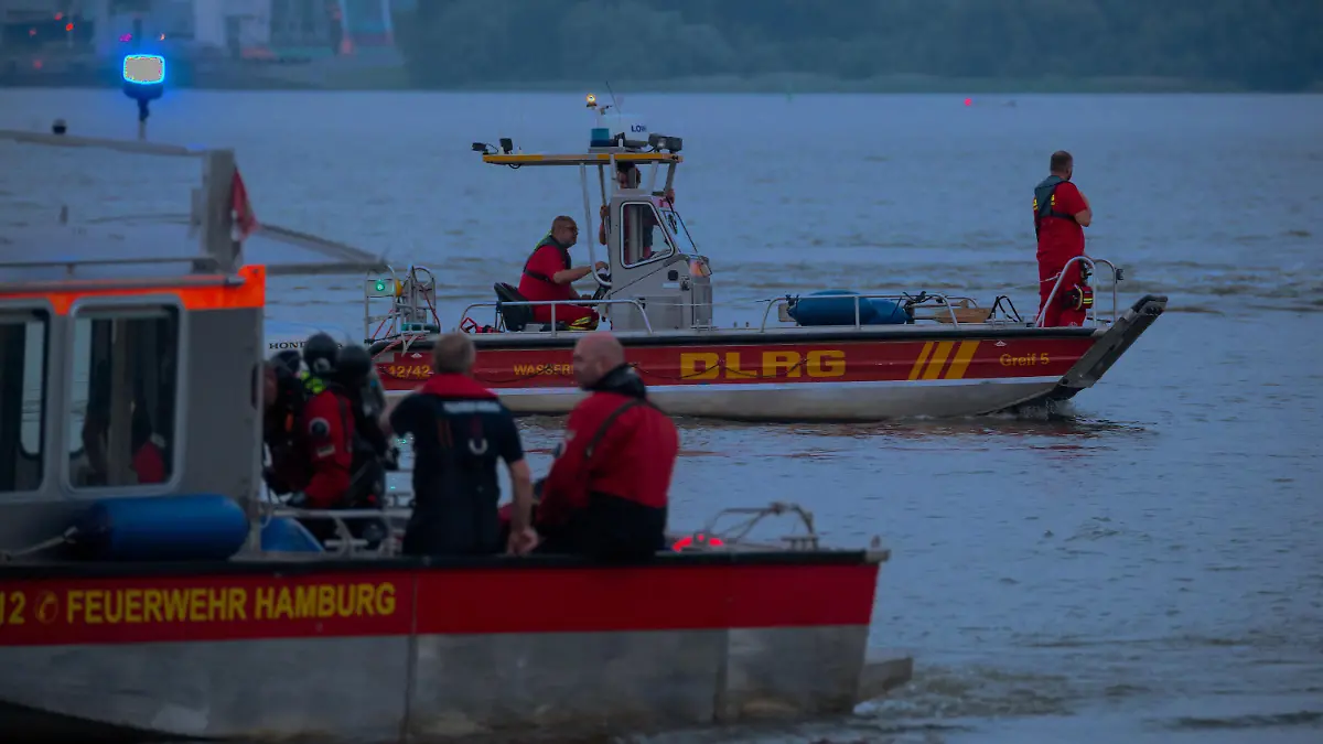 18.06.2021, Hamburg: Kleinboote von DLRG und Feuerwehr fahren bei der Suche über die Elbe. Feuerwehr und Polizei haben am Abend zweieinhalb Stunden nach einem jungen Mann gesucht, der von einem Signalturm in die Elbe gesprungen und nicht mehr aufgetaucht war. Sein Begleiter konnte laut Polizei aus dem Wasser gerettet werden. Foto: Jonas Walzberg/dpa +++ dpa-Bildfunk +++