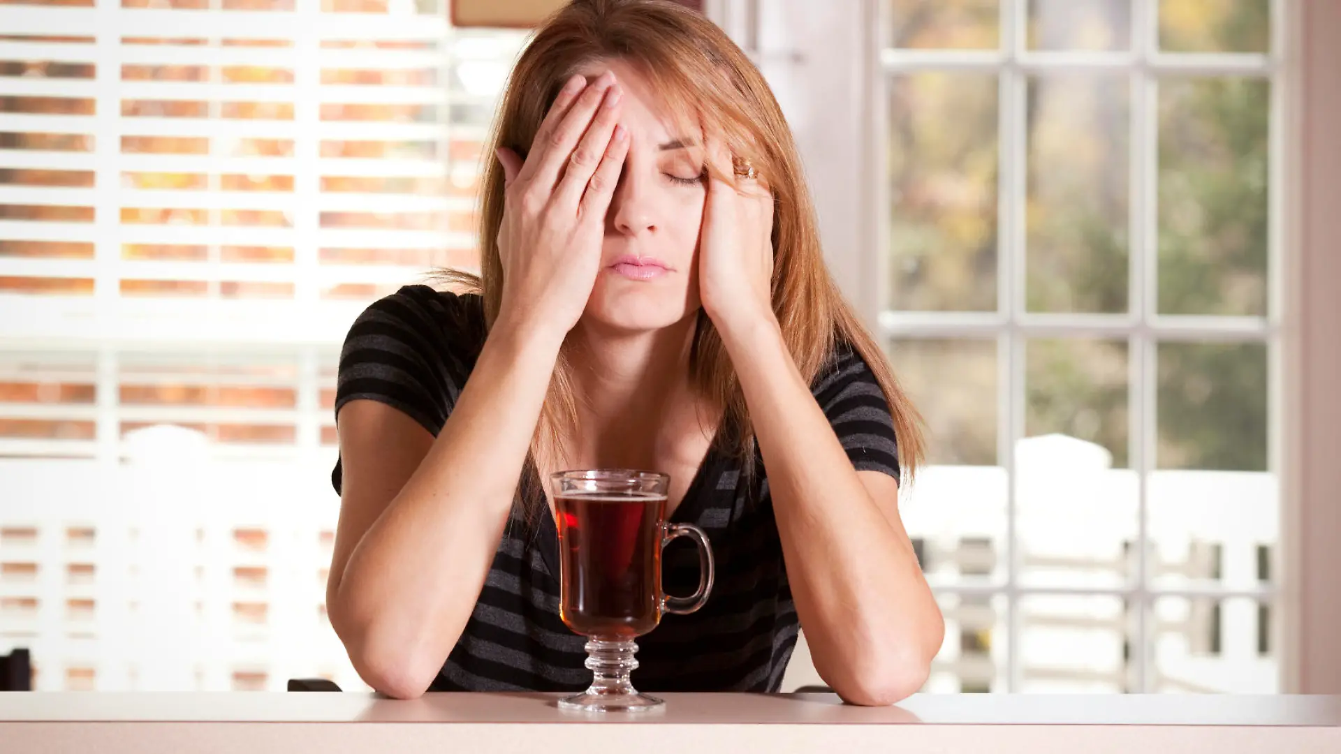 A woman with a cup of tea having a hard time waking up in the morning.