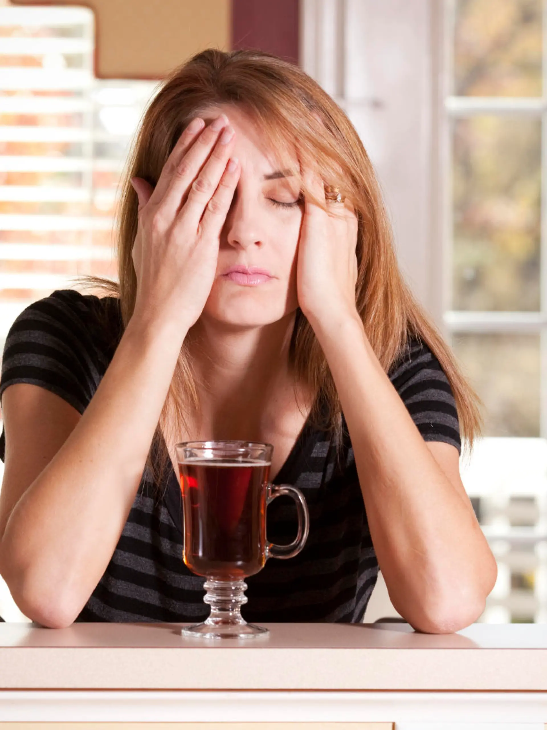 A woman with a cup of tea having a hard time waking up in the morning.