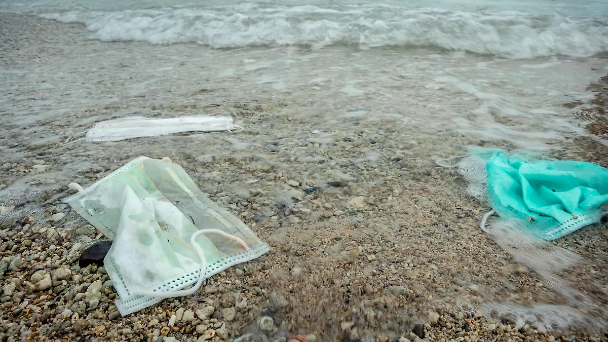 Coronavirus polluting the environment. The waves wash up old used medical mask waste. The personal protective equipment get into the water, they pose a threat to marine life.