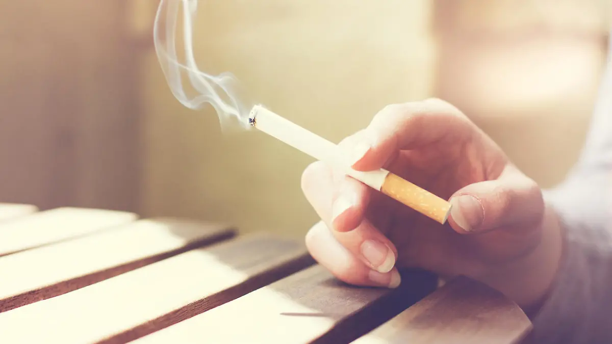 Woman smoker smoking a filter tip cigarette with her hand resting on a slatted wooden table with copy space, close up view