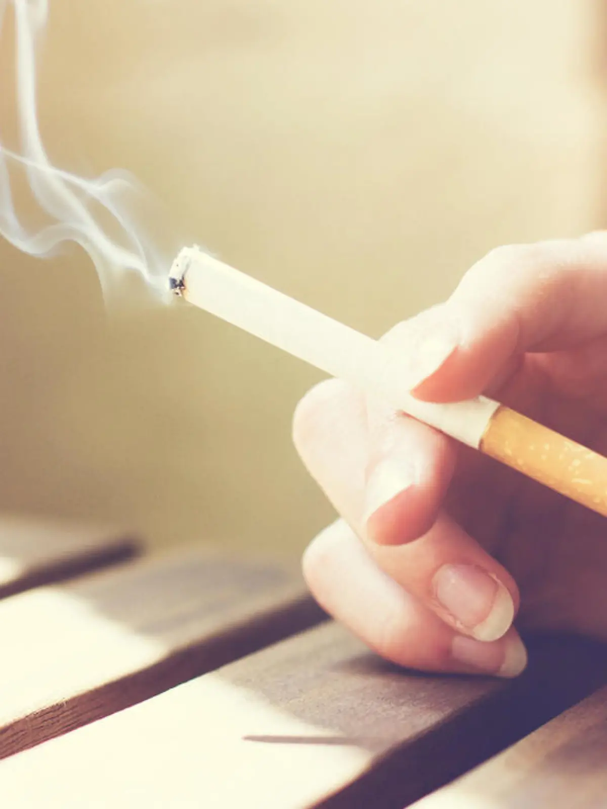 Woman smoker smoking a filter tip cigarette with her hand resting on a slatted wooden table with copy space, close up view