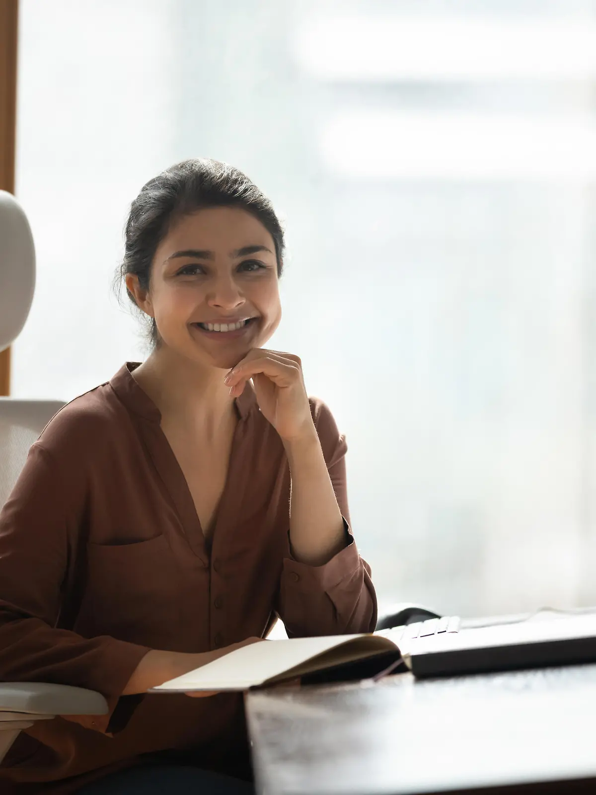 Smiling attractive Indian businesswoman sitting at desk in modern home office pose for camera feel confident, satisfied by business growth. Portrait of female freelancer, motivated student or employee