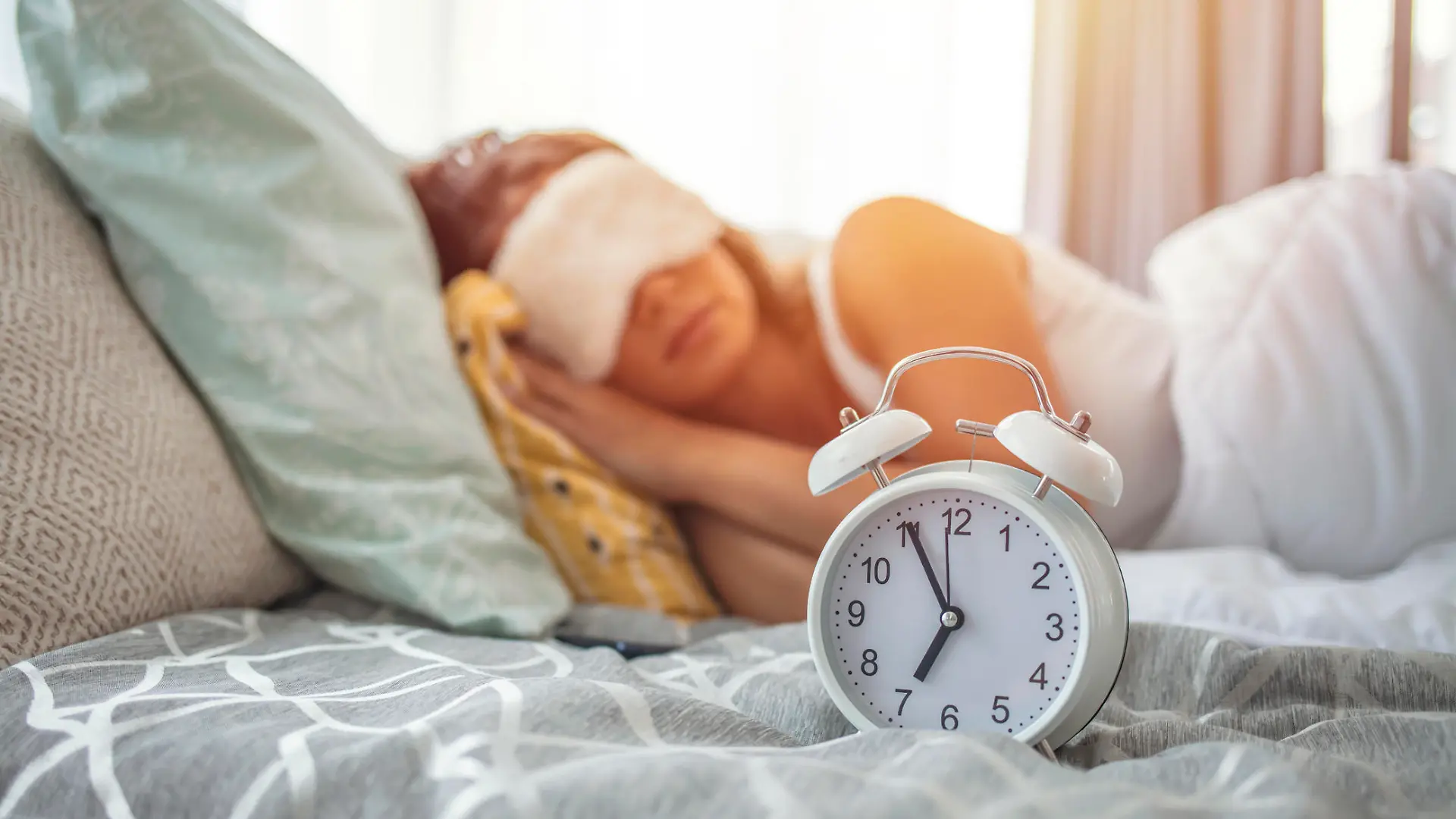 Close up of black alarm clock stand on bedside table show early morning hour, calm peaceful young woman sleep on background relax on fluffy pillow covered with warm blanket in bedroom