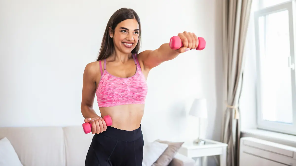 Eine Frau die mit pinken Hanteln ein Arm-Workout macht.