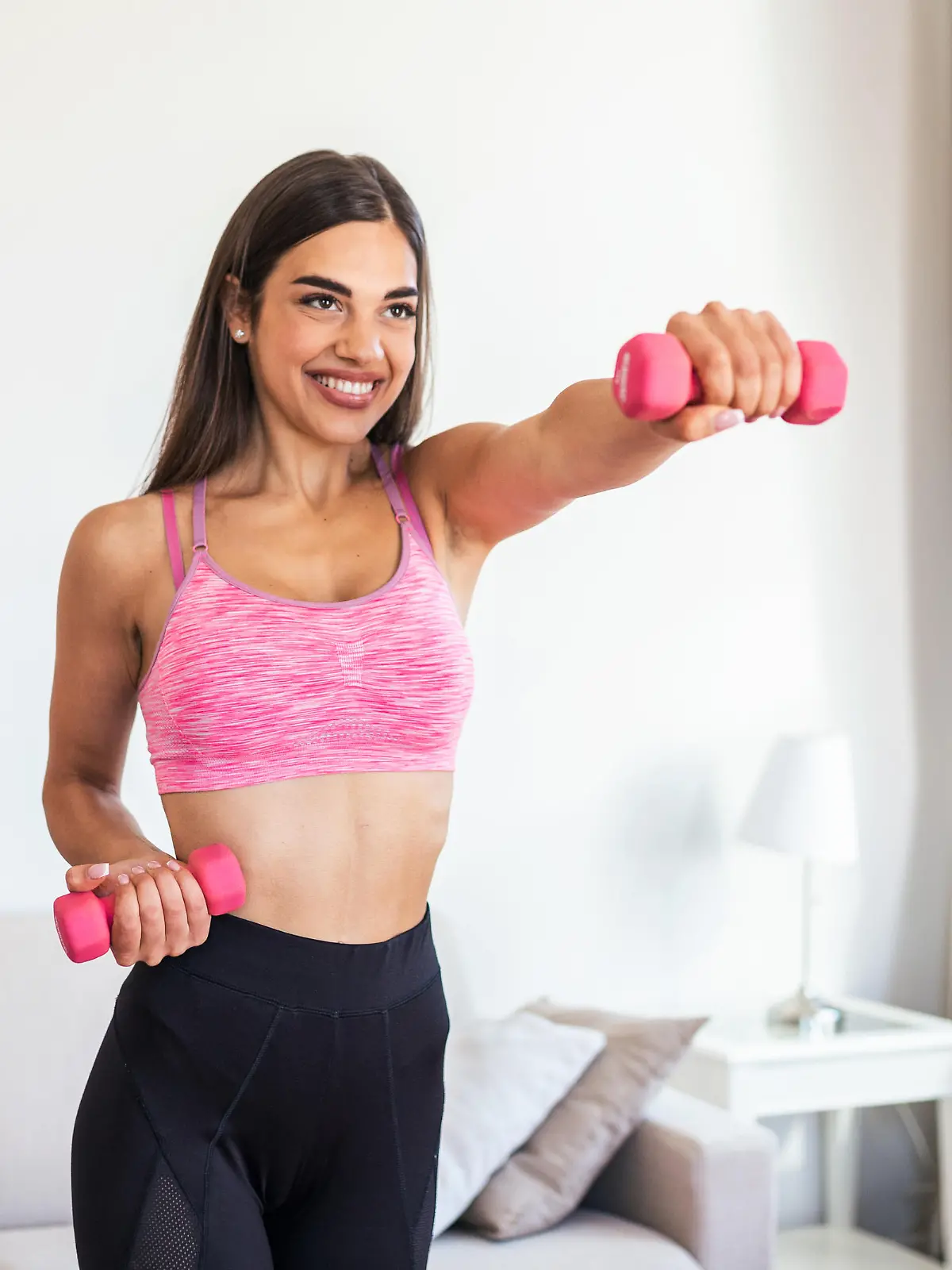 Eine Frau die mit pinken Hanteln ein Arm-Workout macht.
