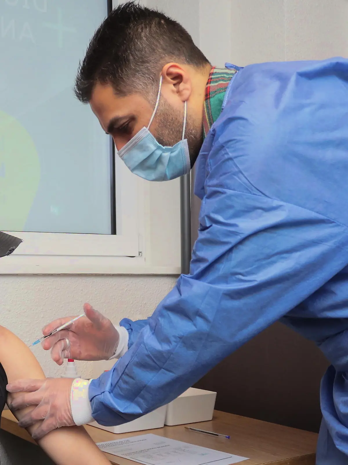 24.12.2021, Nordrhein-Westfalen, Duisburg: Luke van B. (23, l) wird bei einem Weihnachts-Impfmarathon in einem Hotel von Arzt Ahmad-Mujtaba Mostakiem mit dem Biontech-Impfstoff gegen  Corona geimpft. Ahmad-Mujtaba Mostakiem ist eigentlich Neurologe und will in einem Drei-Schicht-System 81 Stunden lang durchimpfen. Impflinge können ohne Anmeldung kommen. Foto: David Young/dpa +++ dpa-Bildfunk +++