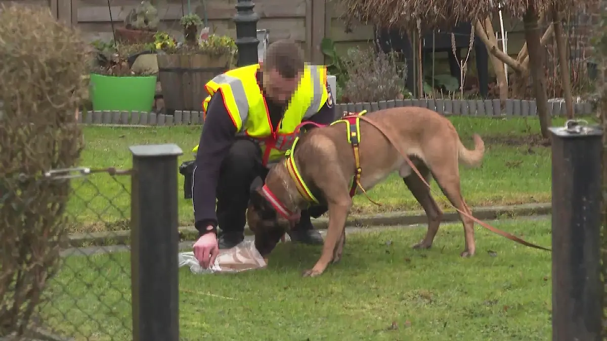 Polizisten haben das Paket, das der Angreifer dabei hatte, in eine Plastikhülle getan und nach draußen gebracht. Ein Polizeihund soll die Witterung aufnehmen.