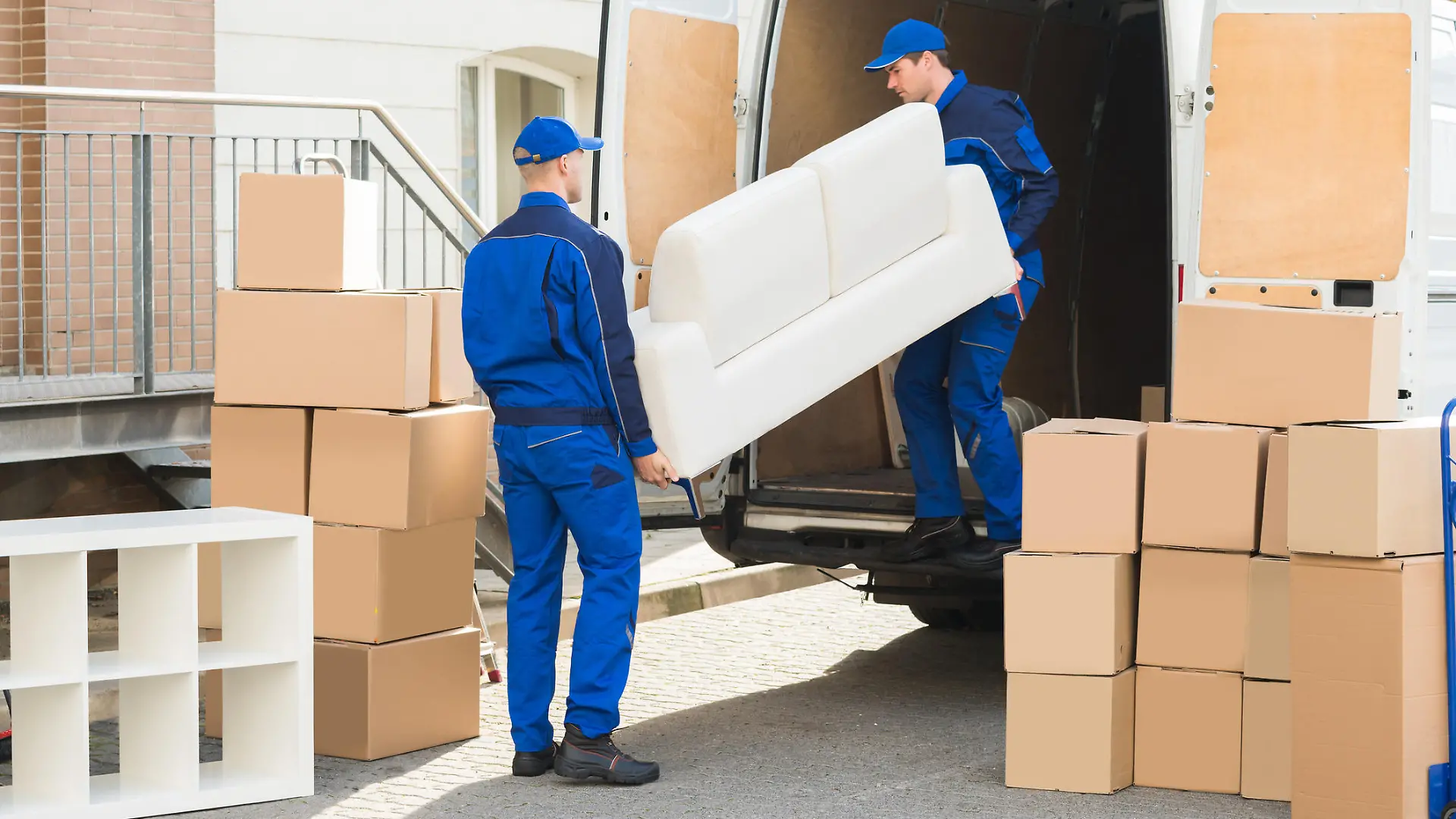 Young male movers unloading sofa from truck on street