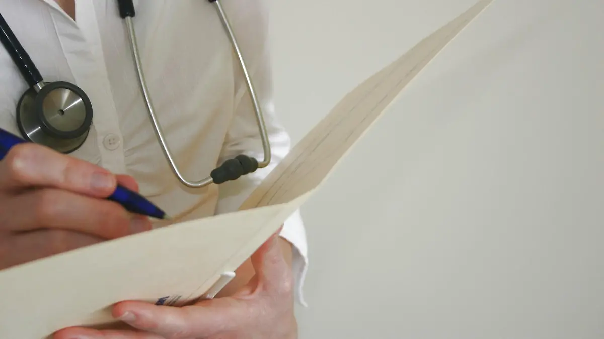 Closeup of female doctor (Caucasian) with stethoscope writing in patient chart