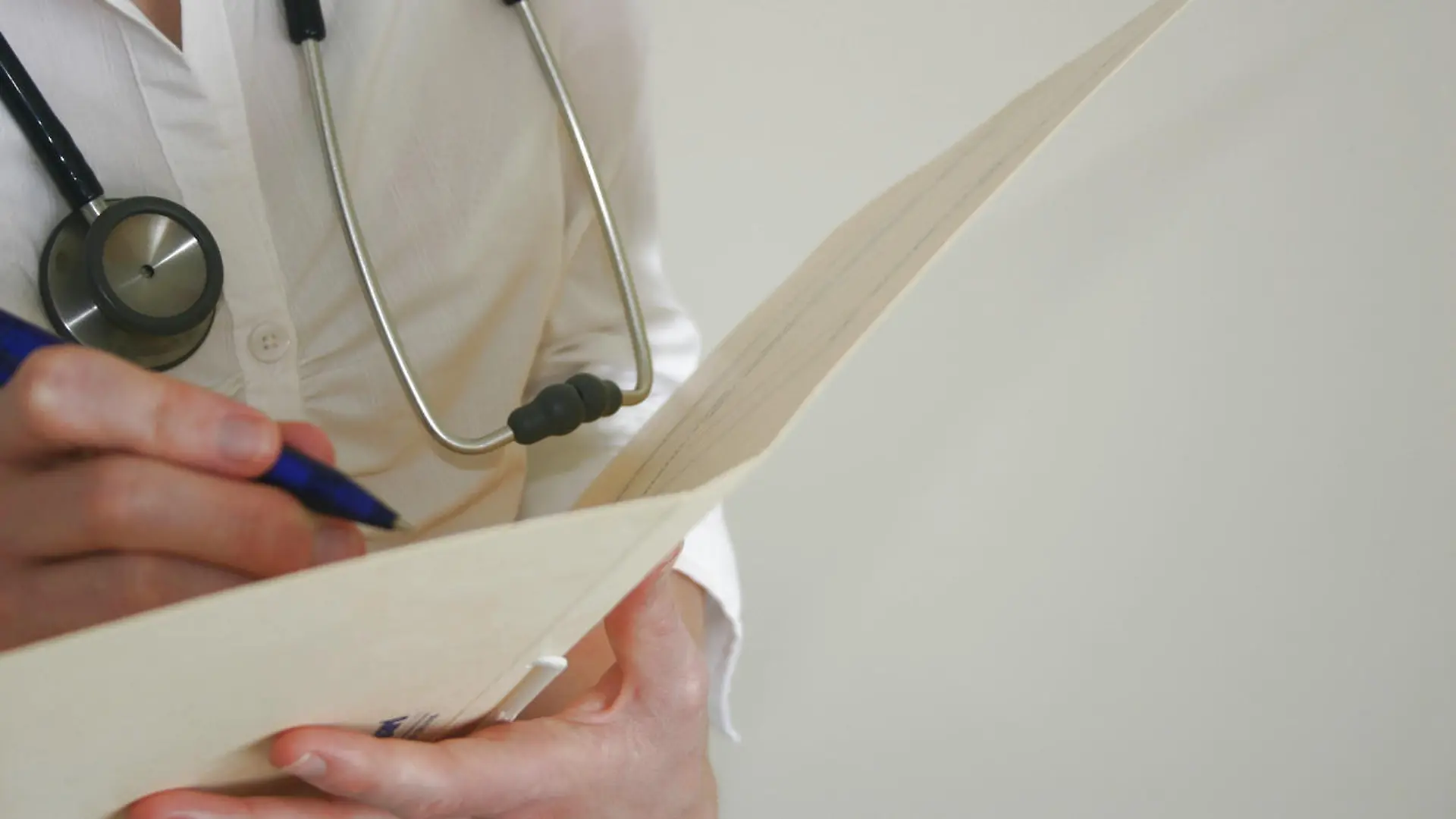Closeup of female doctor (Caucasian) with stethoscope writing in patient chart