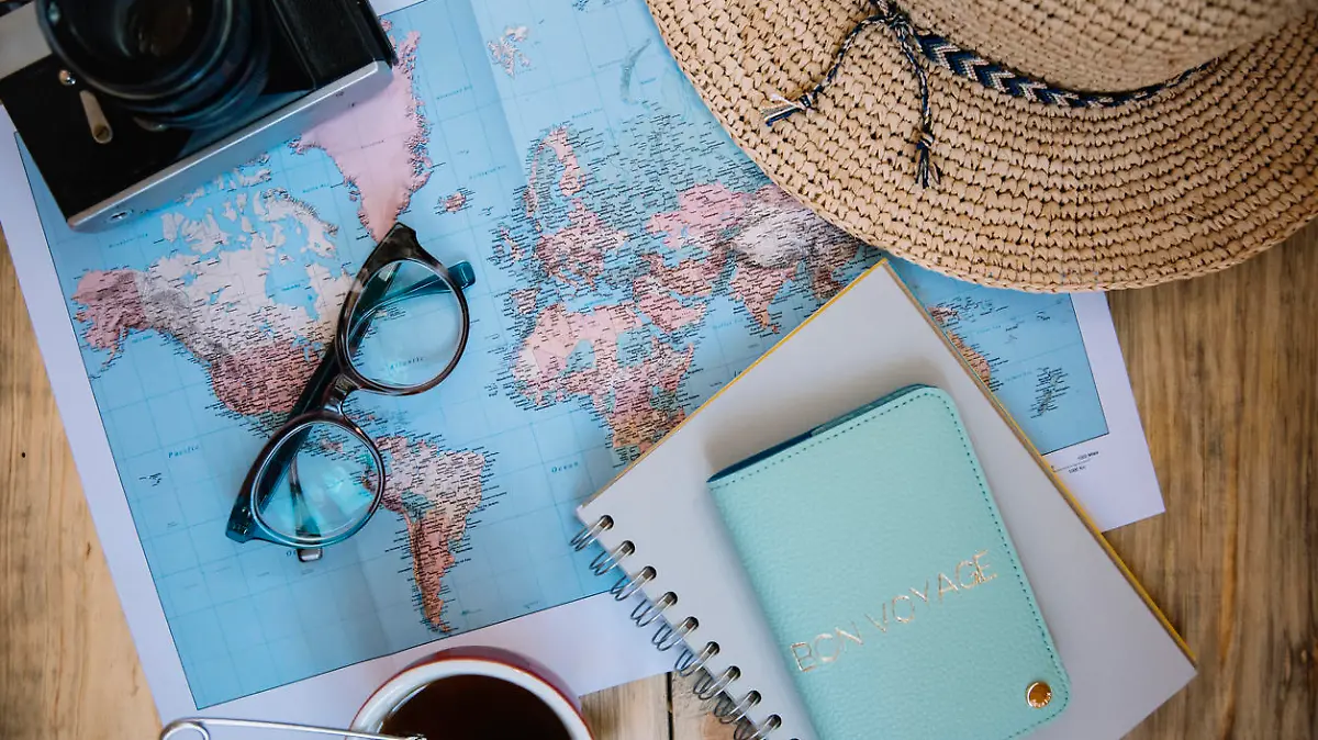 Travel preparations essentials. World map, cup of tea, vintage film camera, hat, passport, notebook and stylish glasses on the old rustic wooden table background, flat lay
