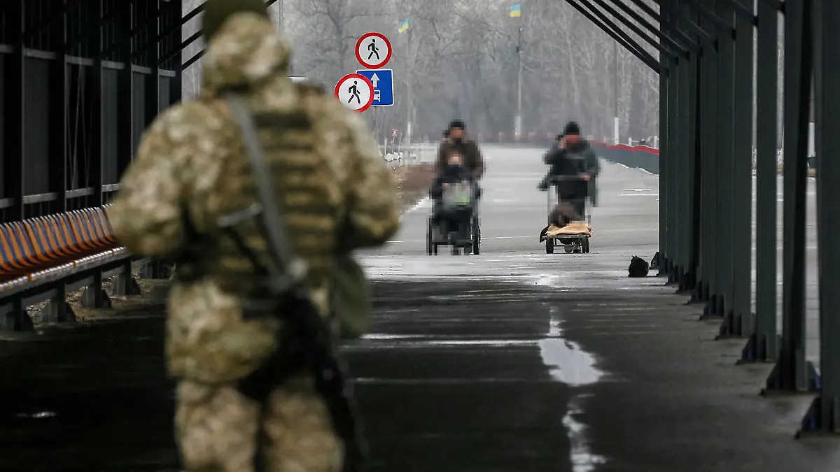 People cross the contact line between pro-Moscow rebels and Ukrainian troops as Ukrainian border guard guards in the settlement of Stanytsia Luhanska, Ukraine February 23, 2022.  REUTERS/Gleb Garanich