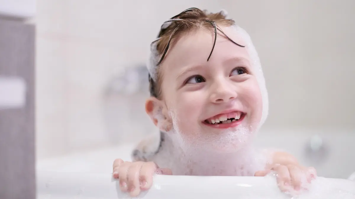 little girl playing with soap foam in bath during coronavirus stay at home pandemic quarantine
