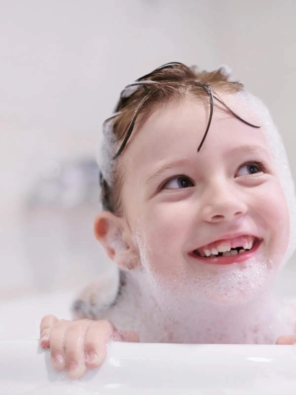little girl playing with soap foam in bath during coronavirus stay at home pandemic quarantine