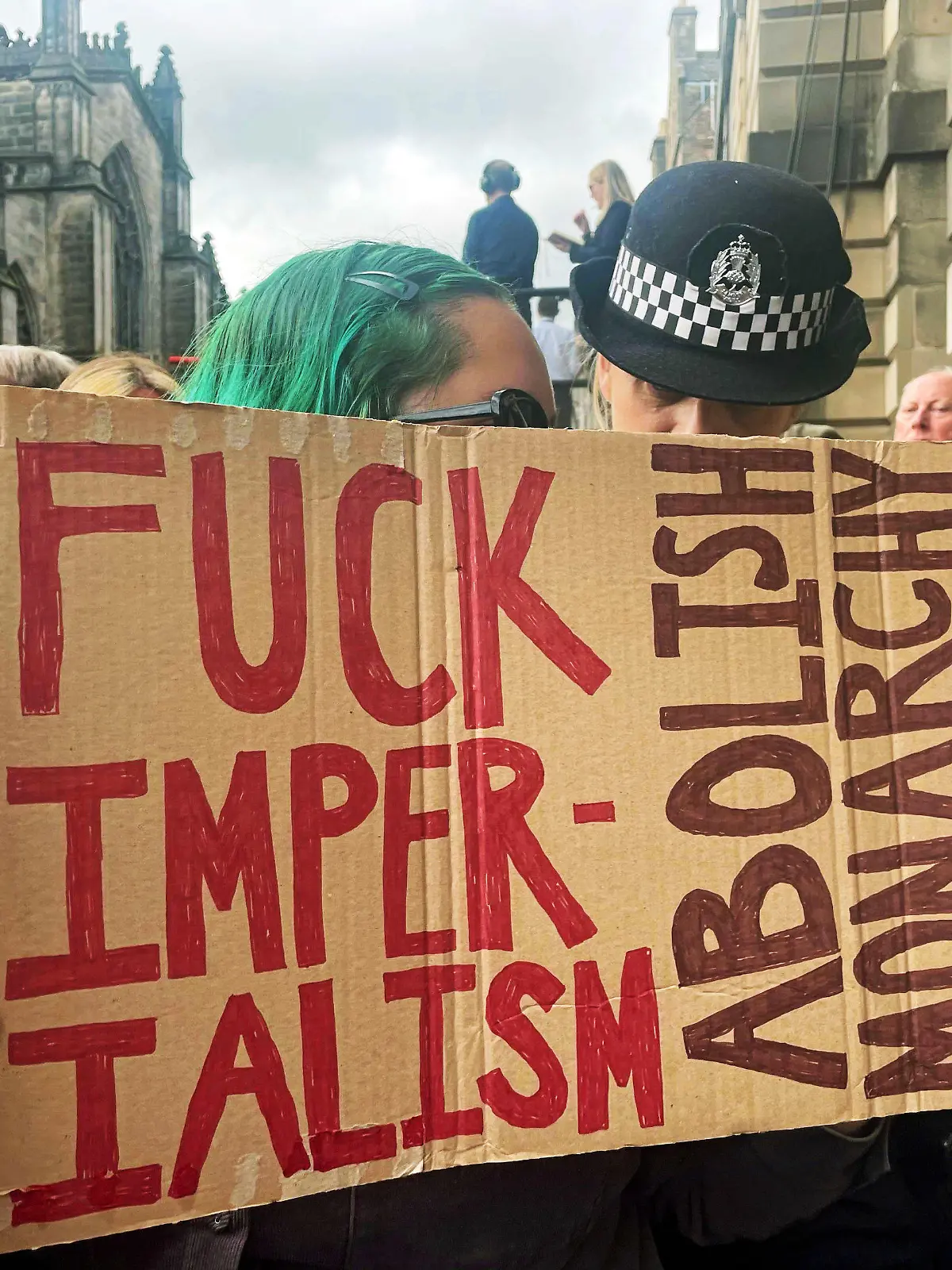 11.09.2022, Großbritannien, Edinburgh: Eine Polizistin spricht mit einer jungen Frau, die ein Schild mit der Aufschrift "Fuck Imperialism - Abolish monarchy" während der Proklamationszeremonie von König Charles III. zur Thronbesteigung am Mercat Cross hält. Es gibt durchaus Briten, die weder mit dem Trubel um den Tod der Queen noch mit der Monarchie insgesamt etwas anfangen können. (zu dpa-Korr "Monarchiegegner und Royal-Muffel: Nicht alle trauern um die Queen") Foto: Isobel Frodsham/PA Wire/dpa +++ dpa-Bildfunk +++