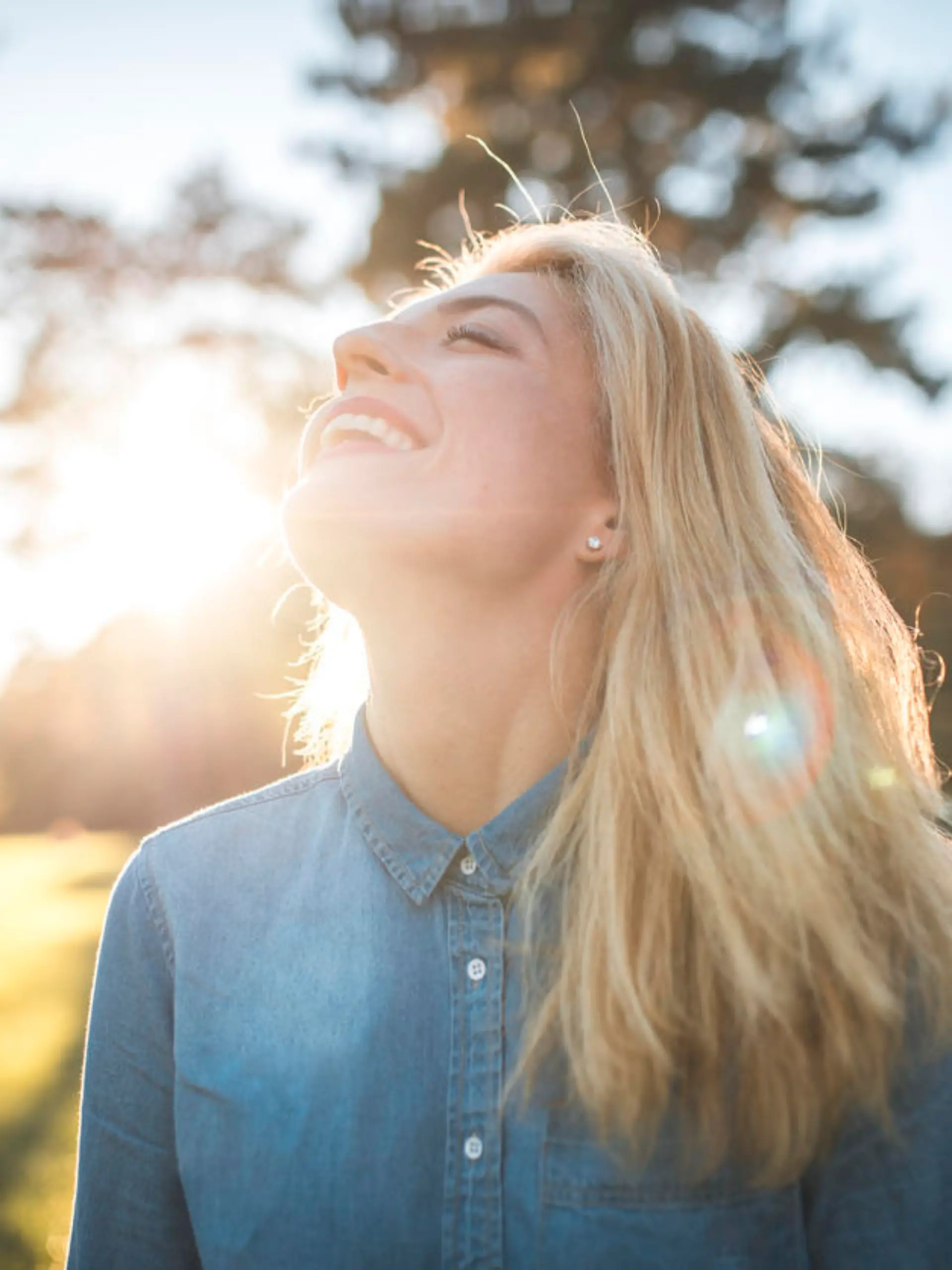 Woman enjoying in a park on a sunny summer day. She have her eyes closed, she is smiling and enjoying fresh air and sun.
