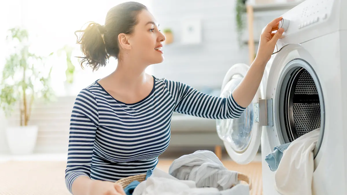 Beautiful young woman is smiling while doing laundry at home.