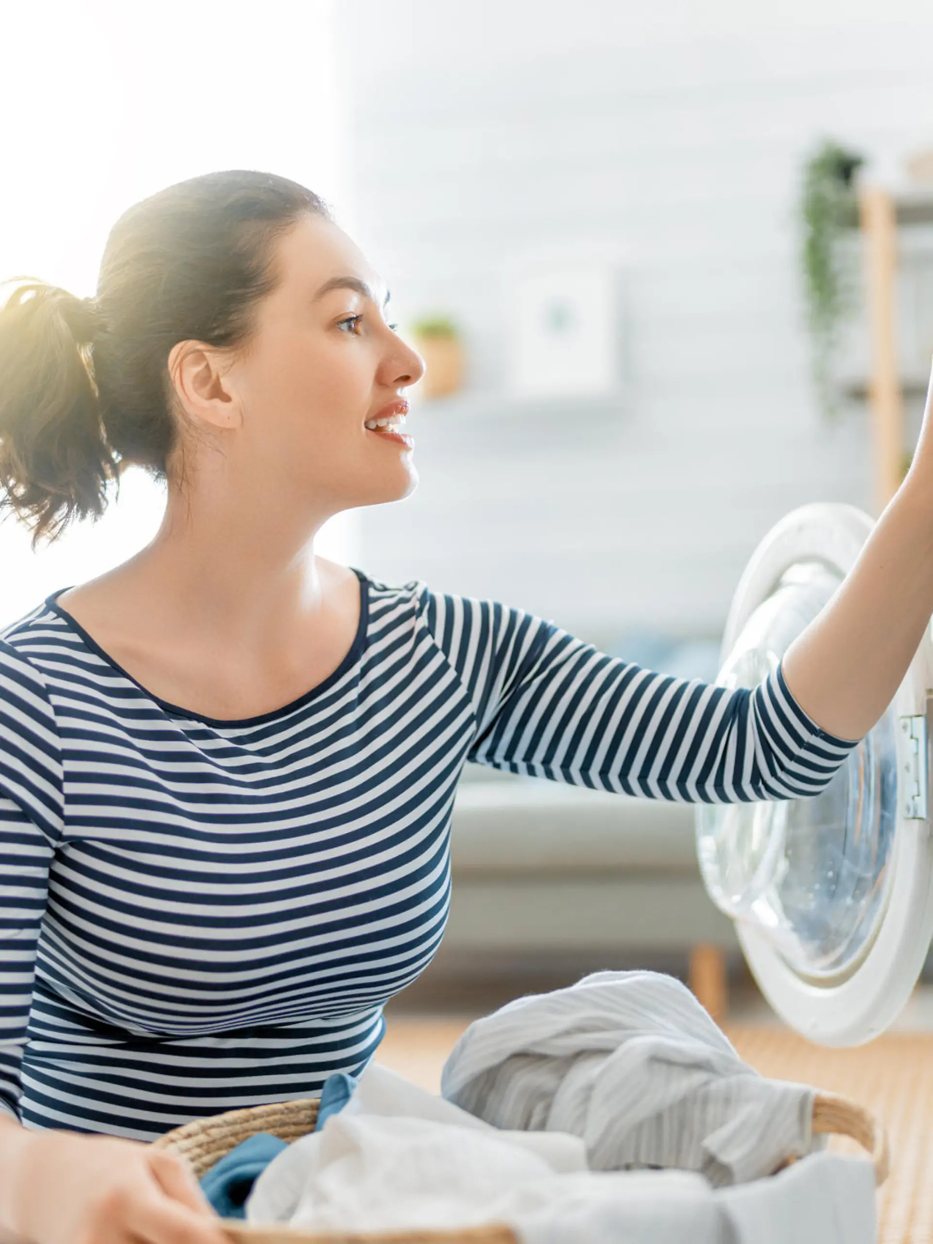 Beautiful young woman is smiling while doing laundry at home.