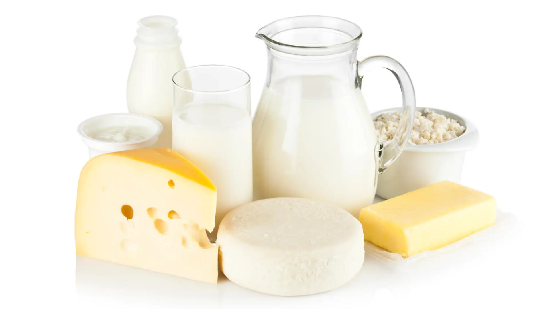 Image of dairy products shot on reflective white backdrop. Includes: milk, various types of cheese, butter, ricotta, milk cream and yogurt. A milk pitcher and a glass of milk are in the center while the rest of the products are around them. A soft shadow is visible in the foreground. The predominant color is white. DSRL studio shot with Canon EOS 5D Mk II