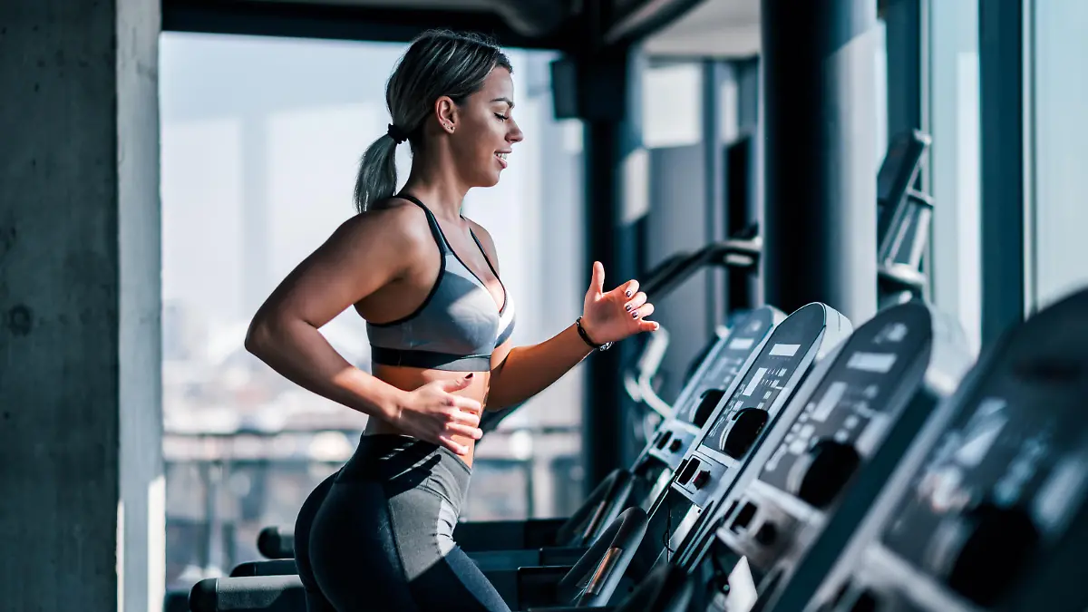 Side view of beautiful muscular woman running on treadmill.