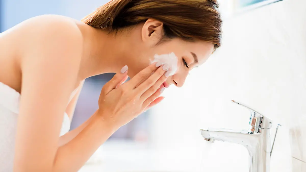 Young woman washing face with clean water in bathroom