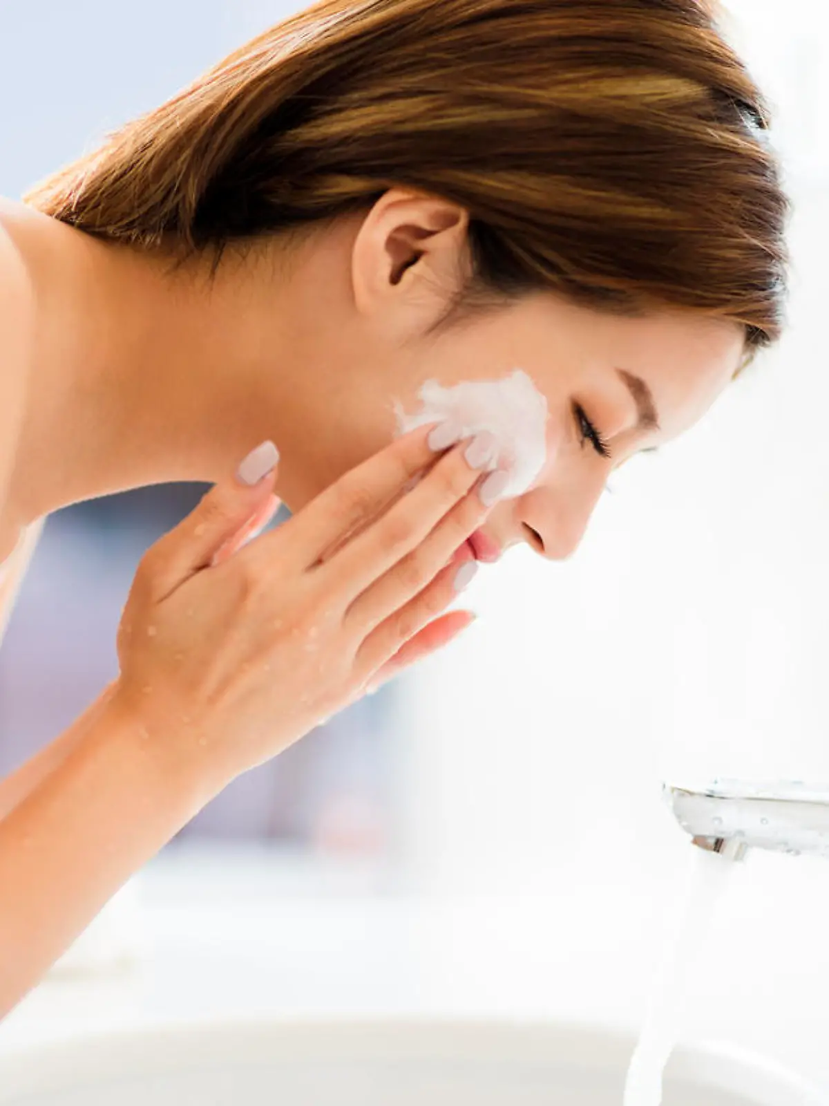 Young woman washing face with clean water in bathroom