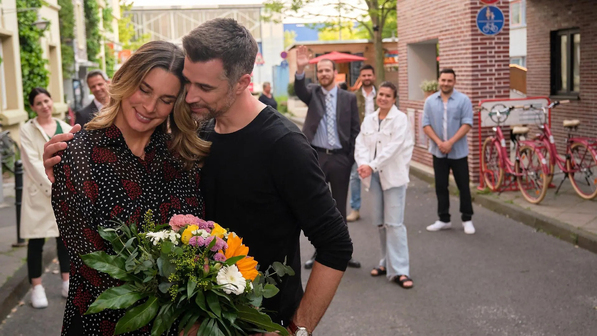 Eva (Claudelle Deckert) schwelgt mit ihrem geliebten Dominic (Jo Weil) im Glück. Die Bewohner der Schillerallee (hinten v.l.: Valea Scalabrino, Jens Hajek, Patrick Müller, Milos Vukovic, Sharon Berlinghoff, Lars Steinhöfel) freuen sich für sie.
Die Verwendung des sendungsbezogenen Materials ist nur mit dem Hinweis und Verlinkung auf RTL+ gestattet.