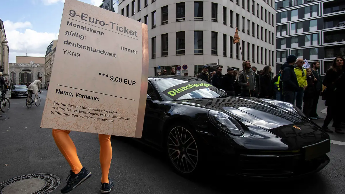18.09.2022, Berlin: «Dienstwagen» steht auf einem Porsche 911 während ein Demonstrant mit einem übergroßen «9-Euro-Ticket» bei einer Protestaktion der Umweltschutz-Organisation Greenpeace vor der FDP-Bundeszentrale daneben steht. Nach Informationen von Greenpeace kostet die Förderung eines Porsche 911 als Dienstwagen dem Staat so viel Geld wie der Zuschuss zu 50 Klimatickets für einen Jahrespreis von maximal 365 Euro. Um das Verhältnis bildhaft zu dokumentieren, hatte Greenpeace auf der gesperrten Reinhardtstraße auf einer Fahrspur den pkw platziert, auf der anderen Seite standen die Aktivisten. Foto: Paul Zinken/dpa +++ dpa-Bildfunk +++