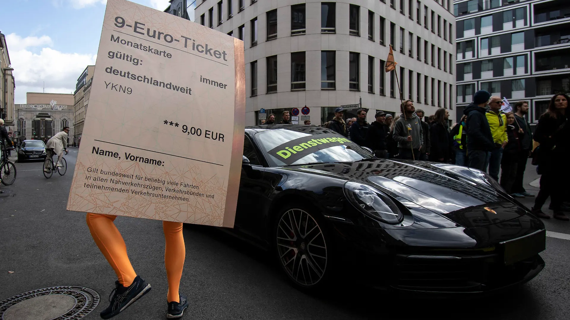 18.09.2022, Berlin: «Dienstwagen» steht auf einem Porsche 911 während ein Demonstrant mit einem übergroßen «9-Euro-Ticket» bei einer Protestaktion der Umweltschutz-Organisation Greenpeace vor der FDP-Bundeszentrale daneben steht. Nach Informationen von Greenpeace kostet die Förderung eines Porsche 911 als Dienstwagen dem Staat so viel Geld wie der Zuschuss zu 50 Klimatickets für einen Jahrespreis von maximal 365 Euro. Um das Verhältnis bildhaft zu dokumentieren, hatte Greenpeace auf der gesperrten Reinhardtstraße auf einer Fahrspur den pkw platziert, auf der anderen Seite standen die Aktivisten. Foto: Paul Zinken/dpa +++ dpa-Bildfunk +++
