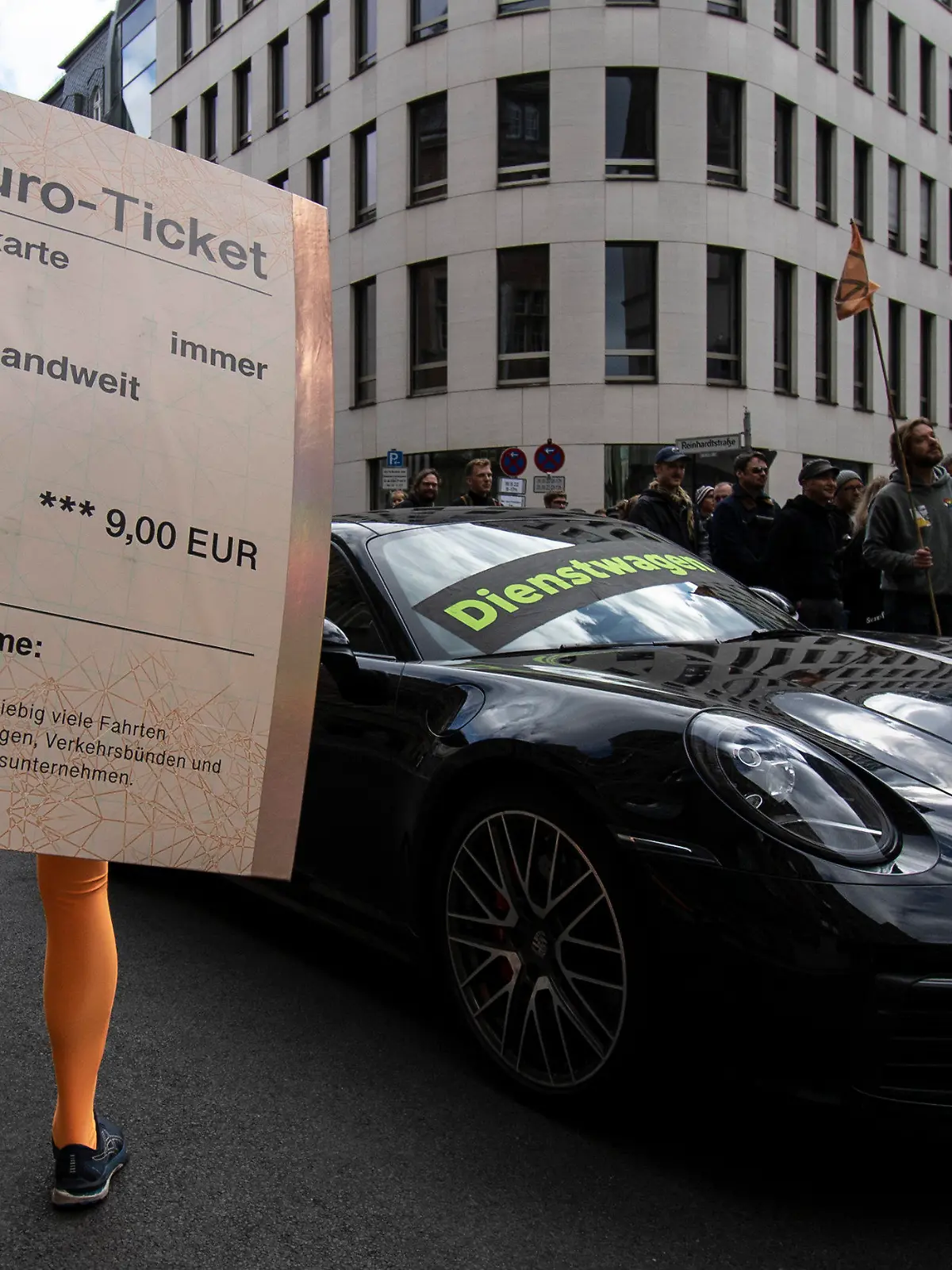18.09.2022, Berlin: «Dienstwagen» steht auf einem Porsche 911 während ein Demonstrant mit einem übergroßen «9-Euro-Ticket» bei einer Protestaktion der Umweltschutz-Organisation Greenpeace vor der FDP-Bundeszentrale daneben steht. Nach Informationen von Greenpeace kostet die Förderung eines Porsche 911 als Dienstwagen dem Staat so viel Geld wie der Zuschuss zu 50 Klimatickets für einen Jahrespreis von maximal 365 Euro. Um das Verhältnis bildhaft zu dokumentieren, hatte Greenpeace auf der gesperrten Reinhardtstraße auf einer Fahrspur den pkw platziert, auf der anderen Seite standen die Aktivisten. Foto: Paul Zinken/dpa +++ dpa-Bildfunk +++