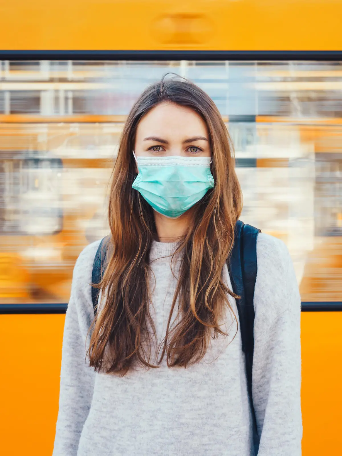 Woman wearing a surgical mask standing in front of the moving train